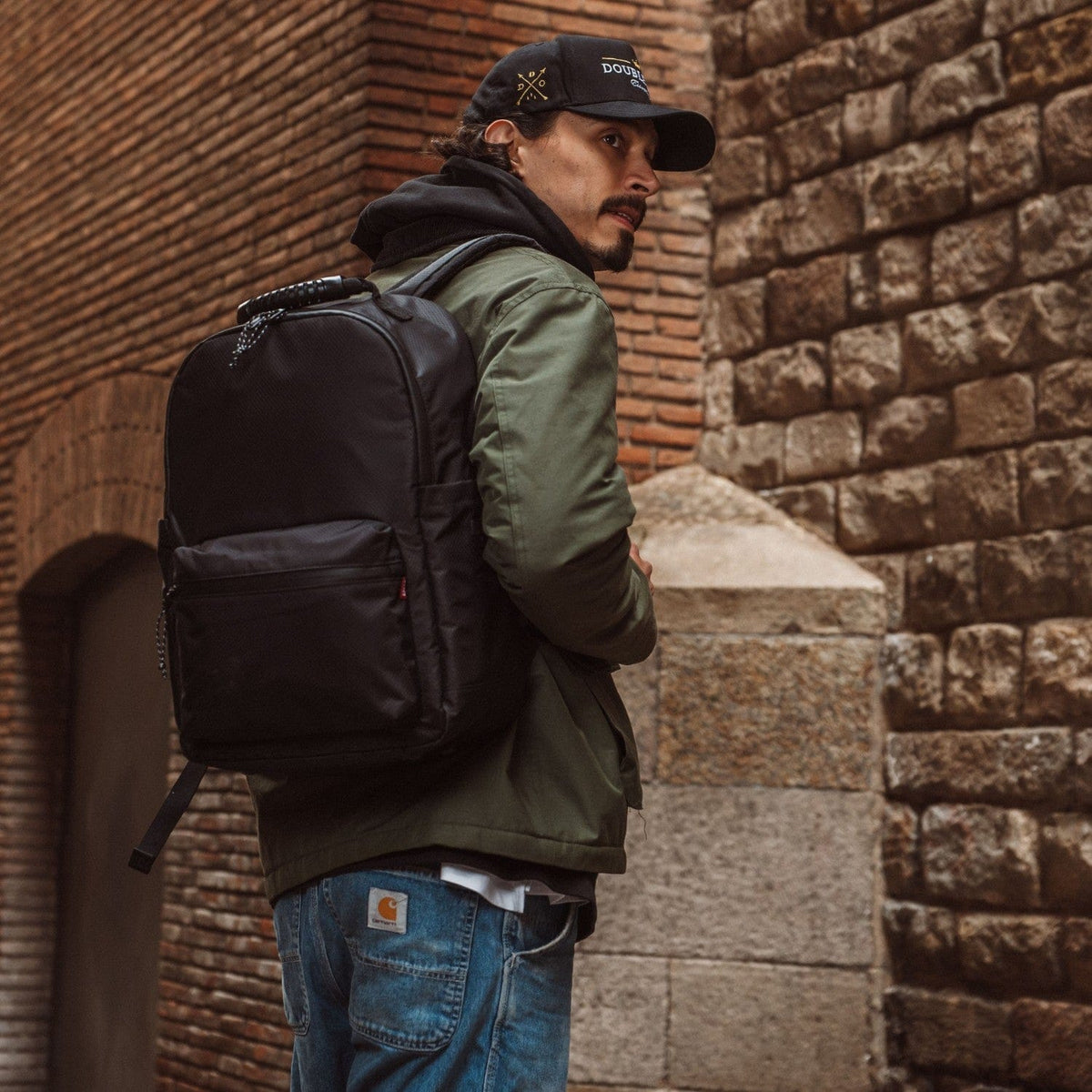 Black and dark green backpack worn on back with side pocket and straps