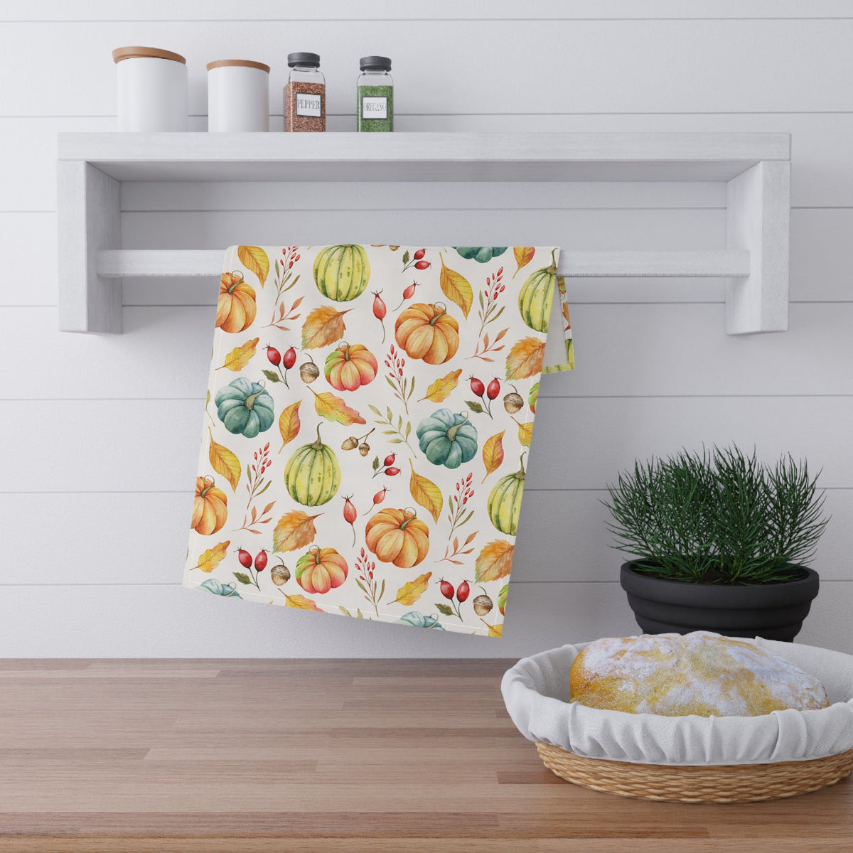 Cream autumn harvest tea towel with pumpkin, leaf, and berry pattern, hanging loop.