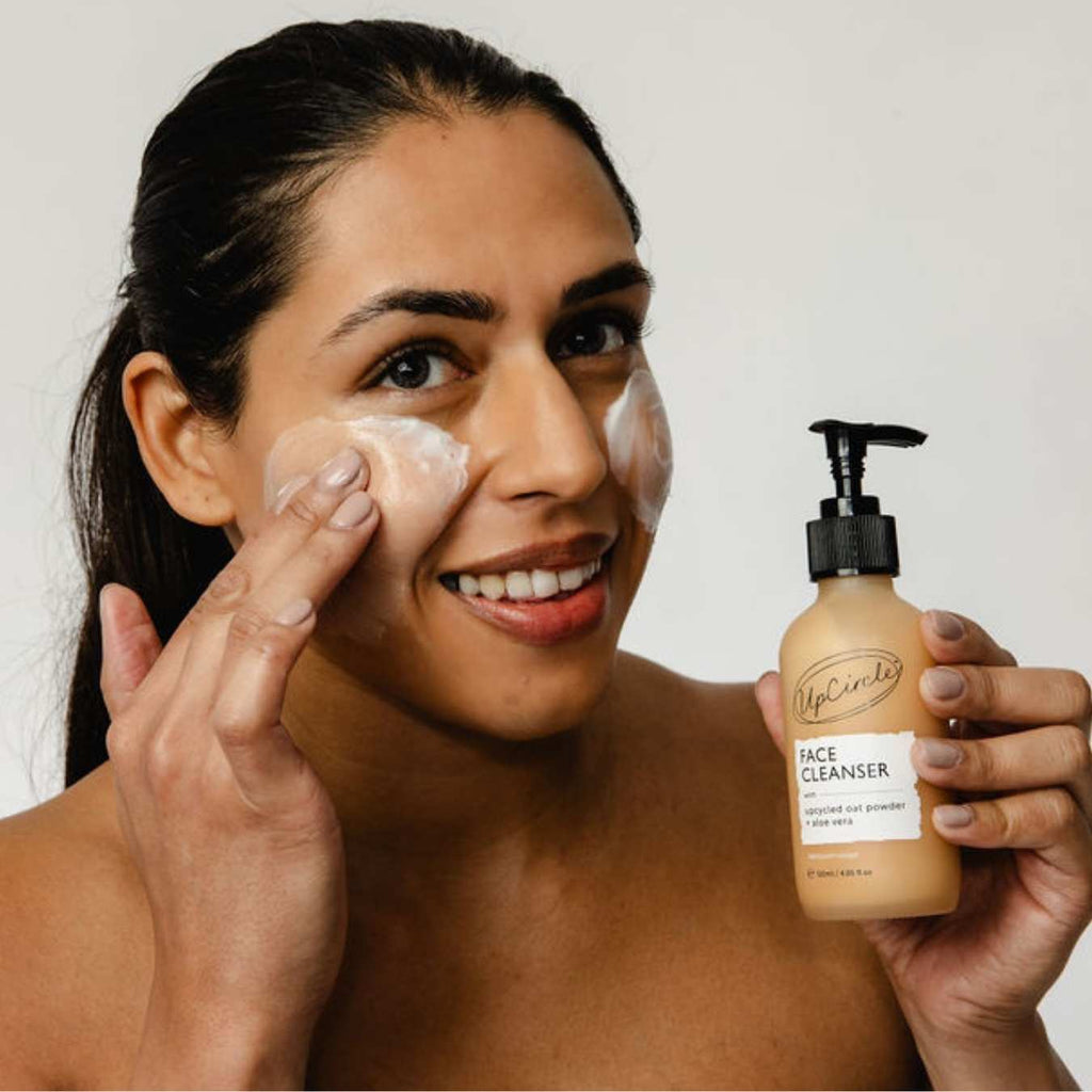 Woman applying cleansing face milk cream while holding the pump bottle
