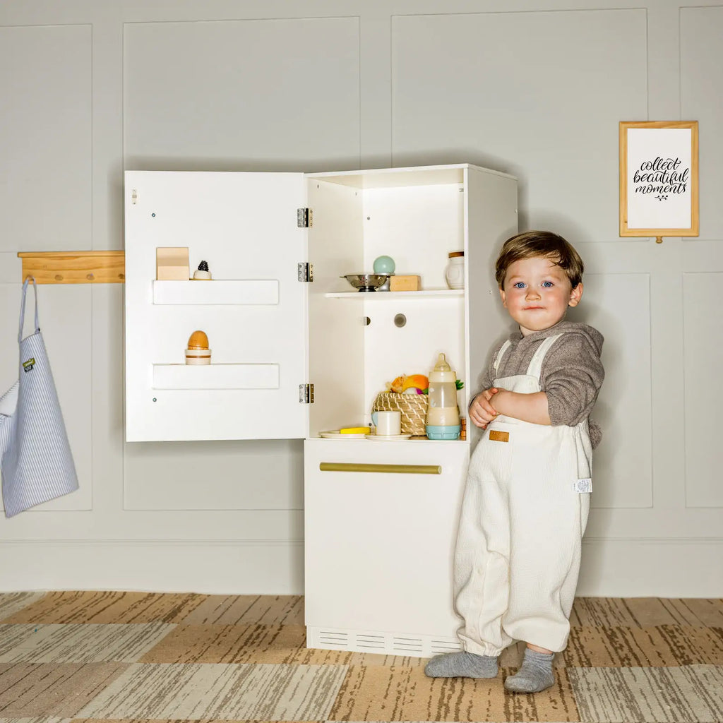 White play kitchen refrigerator cabinet with open doors beside a toddler