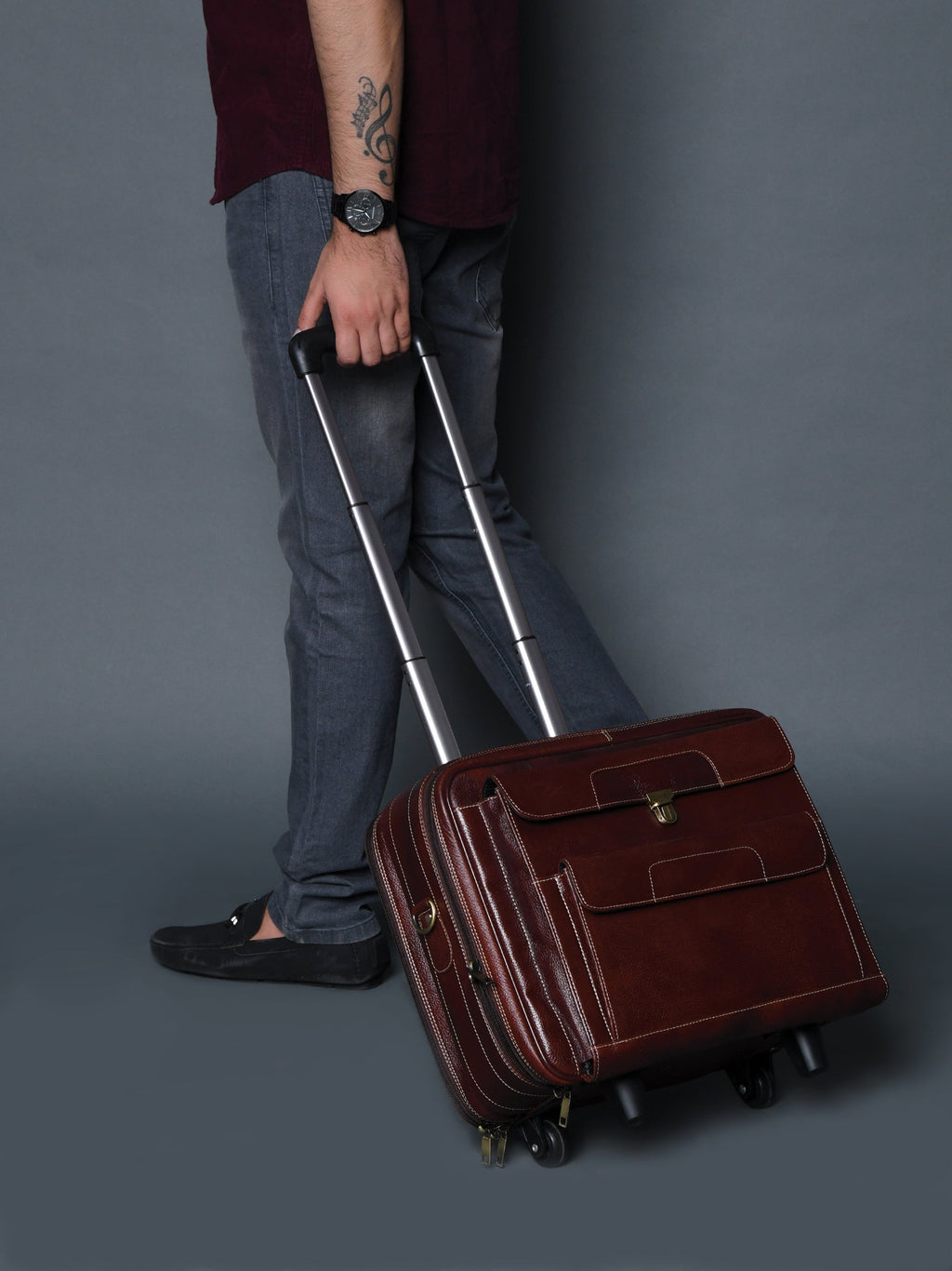 Brown leather trolley suitcase bag tilted on wheels, compact front flap with brass hardware