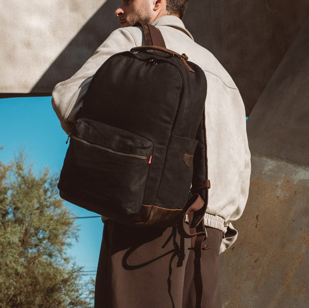 Black fabric backpack with front zip pocket and brown leather straps