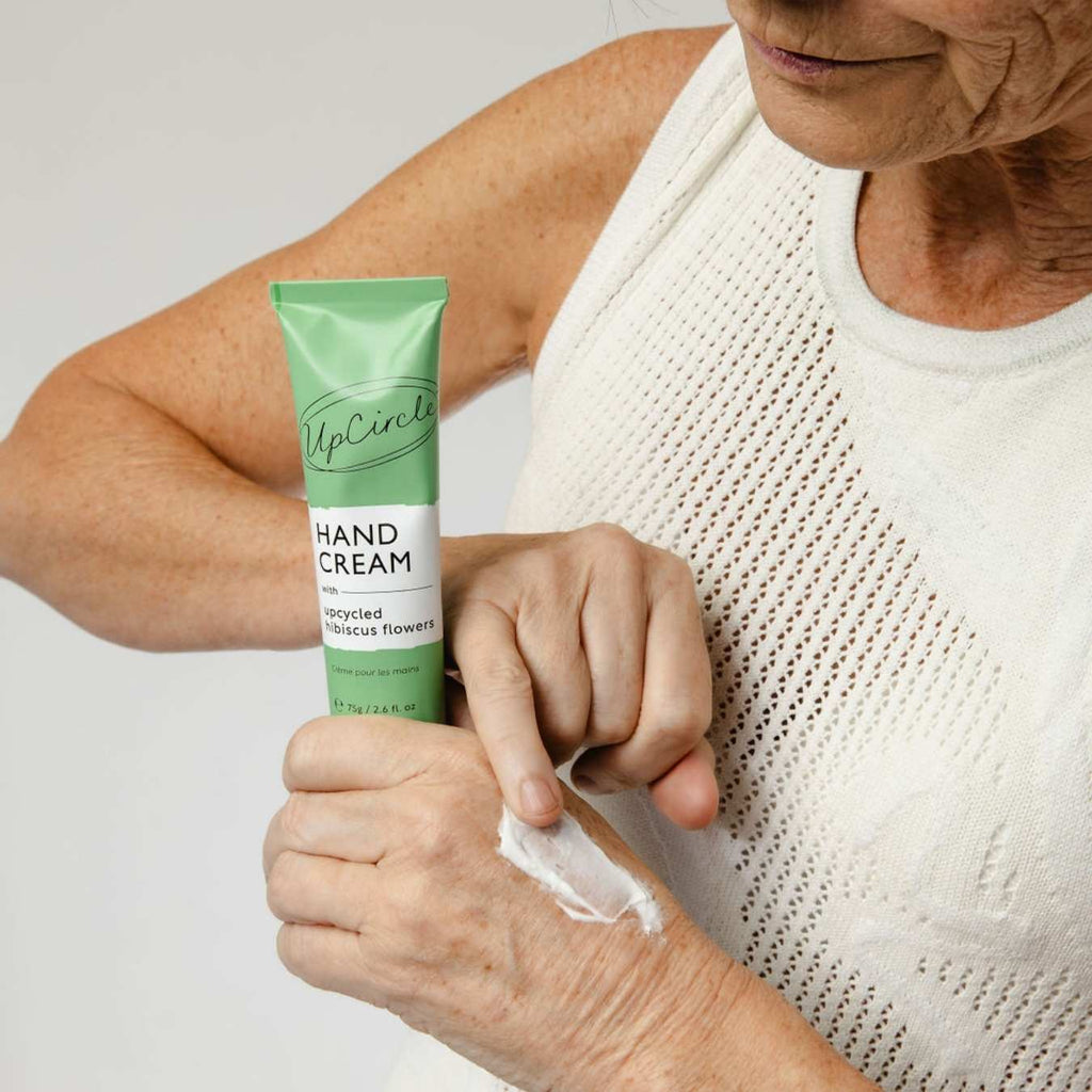 UpCircle green hand cream tube with cream being rubbed on hand