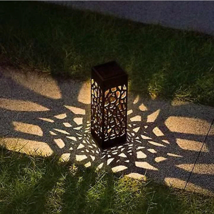Black solar garden lantern light with cutout sides, emitting warm light on ground