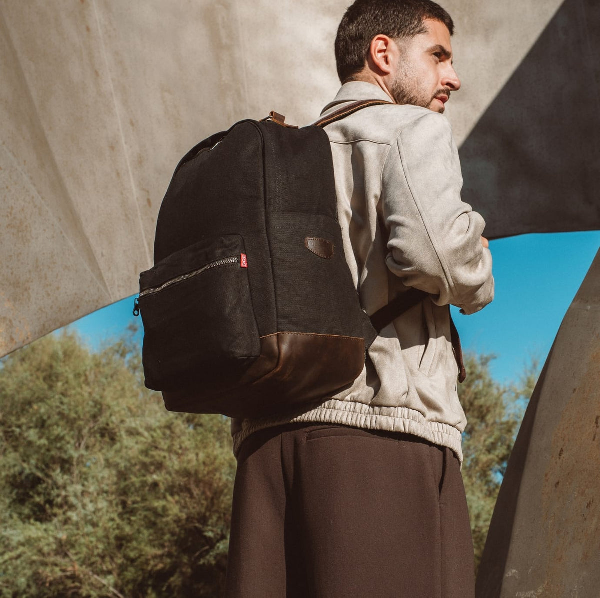 Dark canvas backpack with front zip pocket and brown leather trim