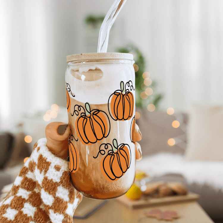 Hand holding frosted glass tumbler with orange pumpkin print, bamboo lid and straw