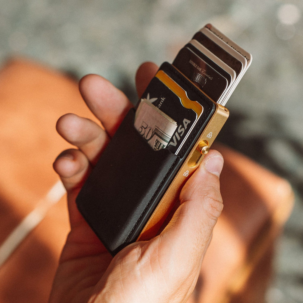 Black leather cardholder wallet with cards and gold hardware, held in hand.