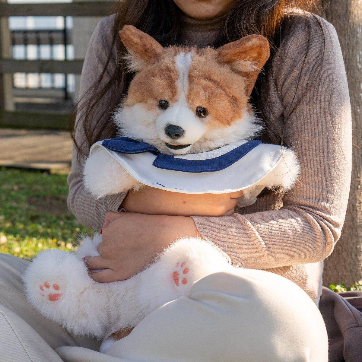 Corgi plush backpack held in arms, with navy bow collar and plush paw prints