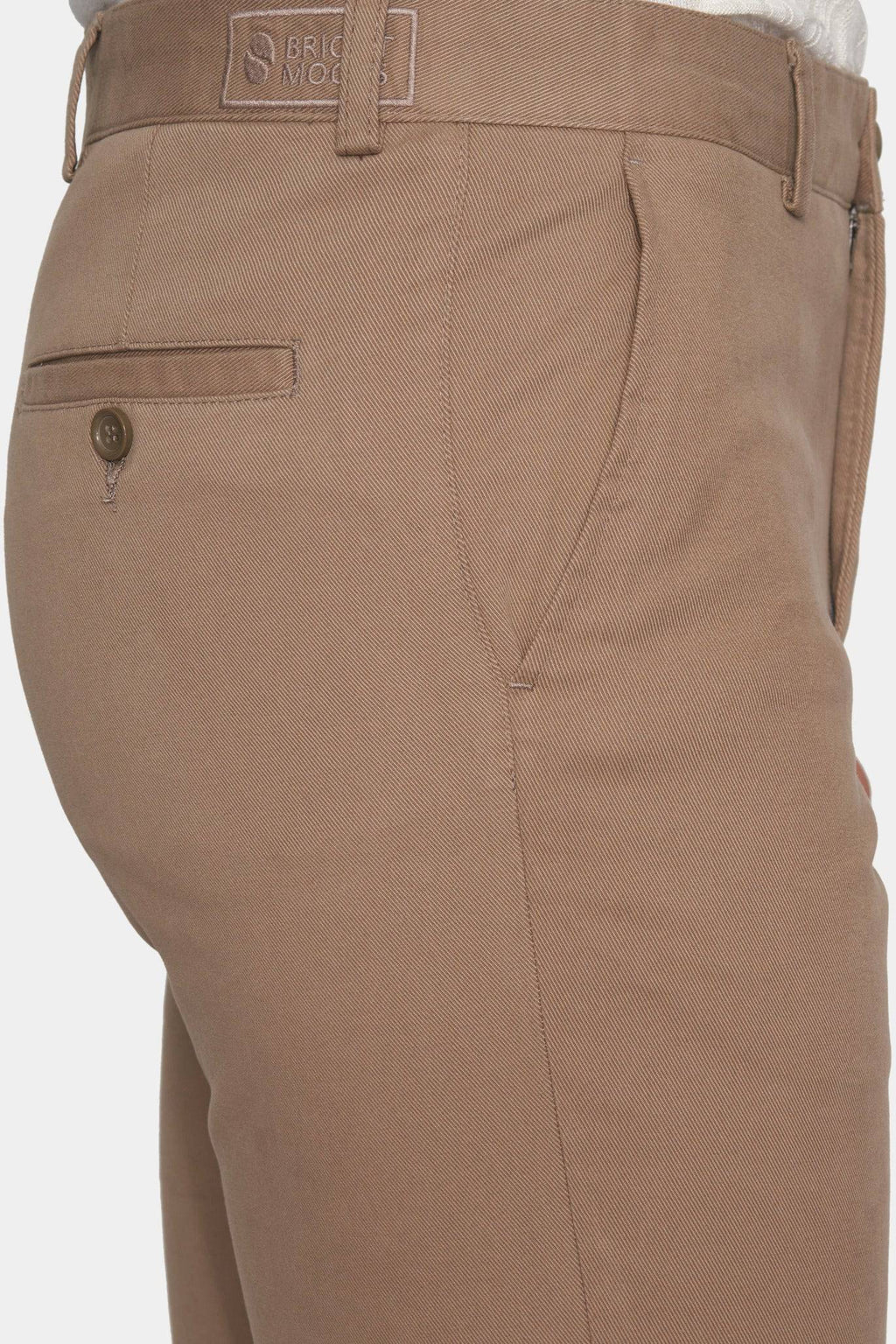 Tan chino pants close-up: logo label, front pocket, and zip-fly seam
