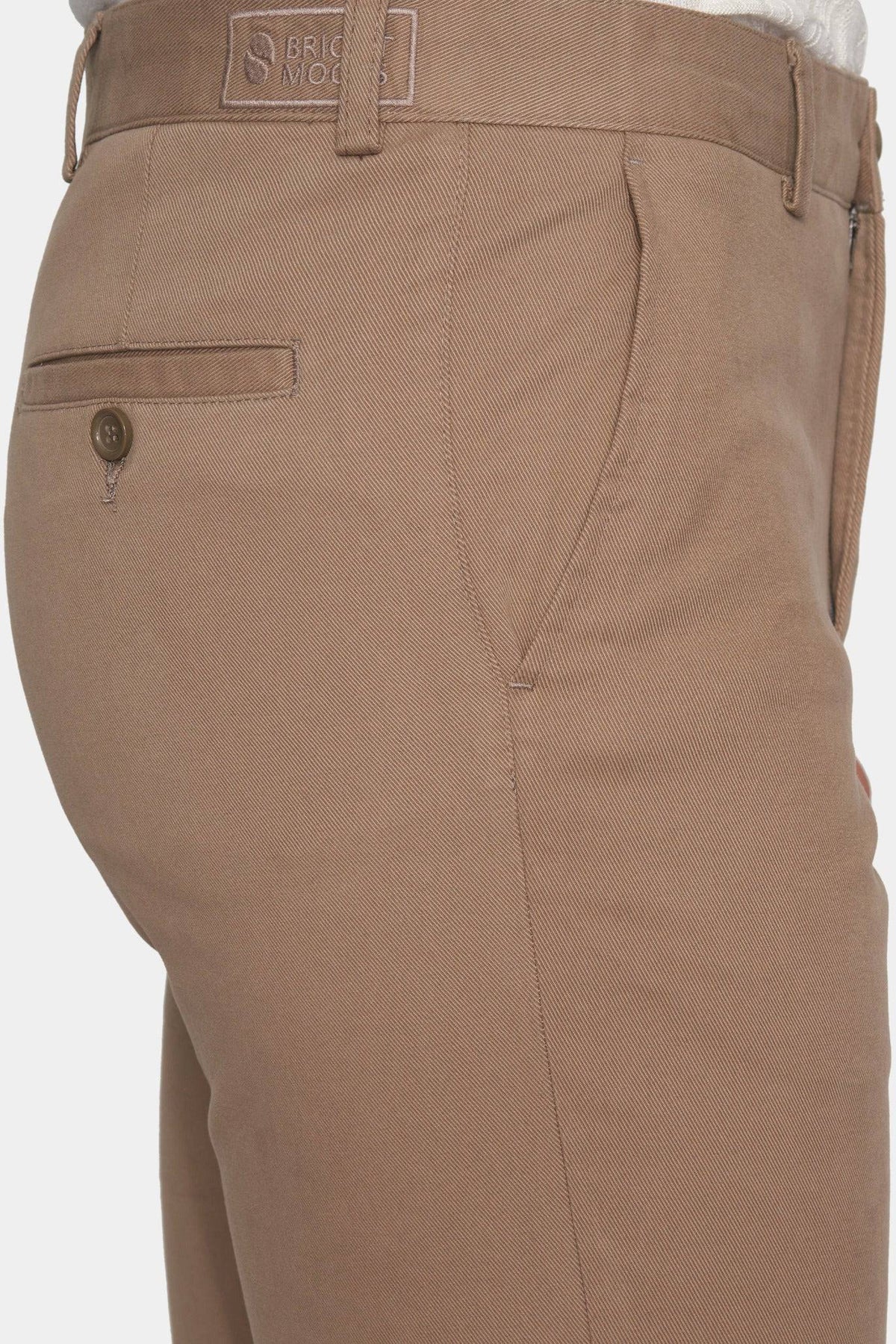 Tan chino pants close-up: logo label, front pocket, and zip-fly seam