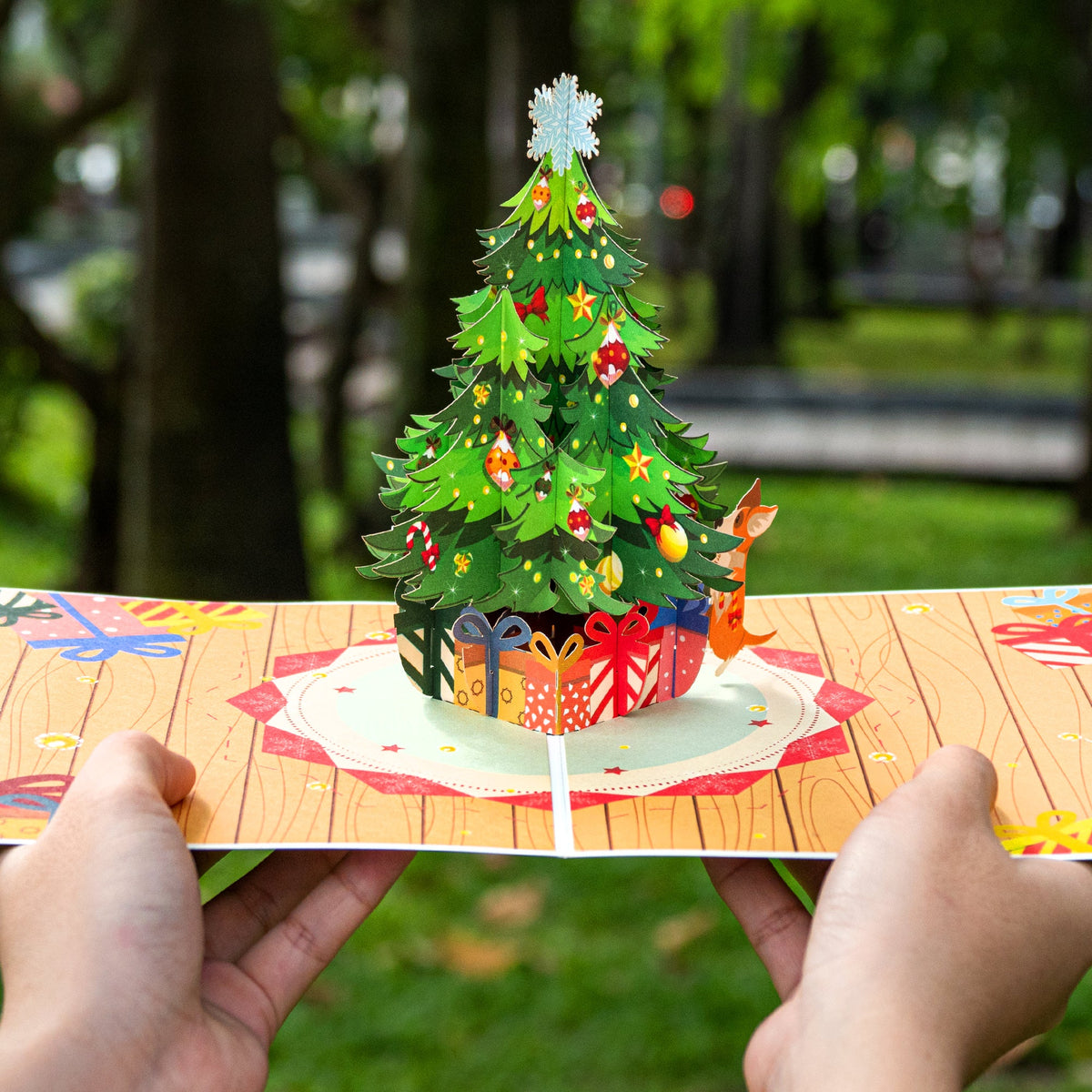 Open pop-up Christmas tree card with gift-wrapped base, held by two hands