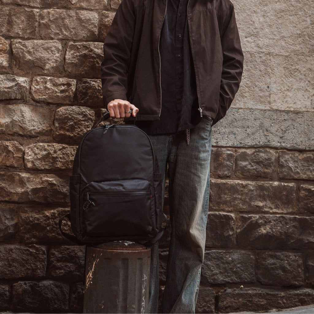Black backpack with top handle, front zip pocket, and flap closure