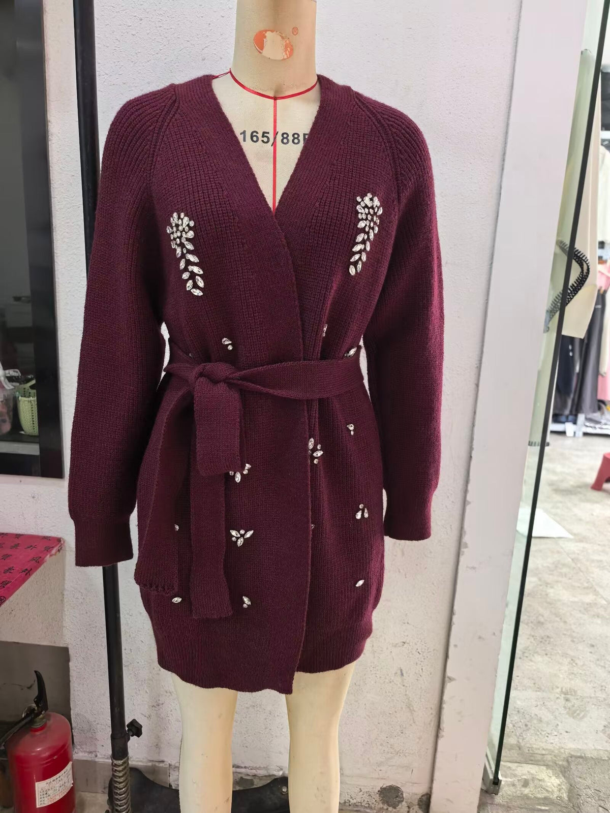 Burgundy knitted cardigan with V-neck, long sleeves, beaded motifs, and waist tie