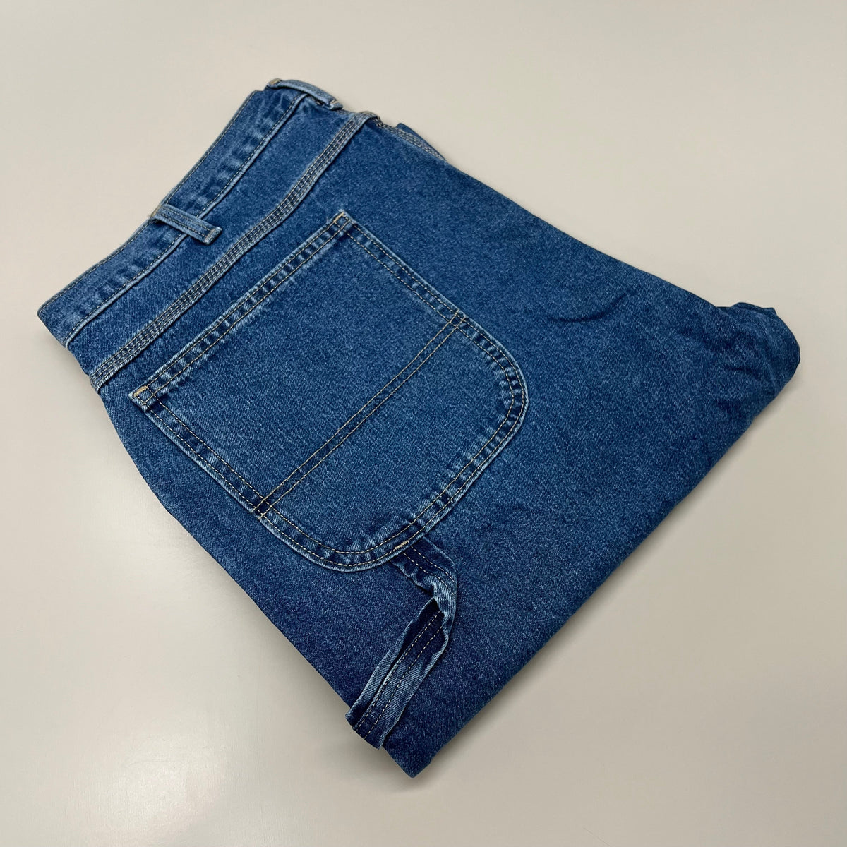 Folded carpenter jeans showing stitched knee and back patch pocket, indigo denim.