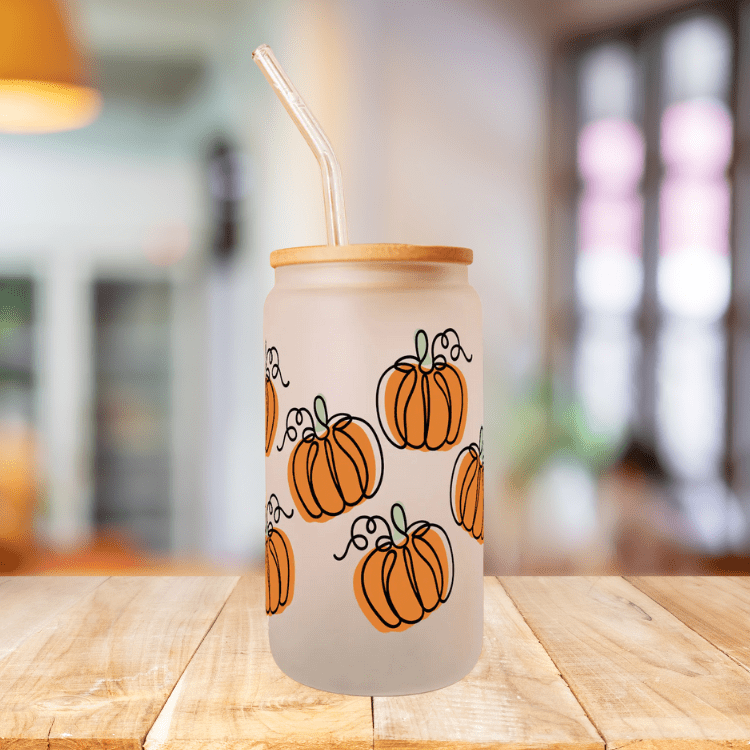 Frosted glass tumbler with orange pumpkin print, bamboo lid and straw on wooden table