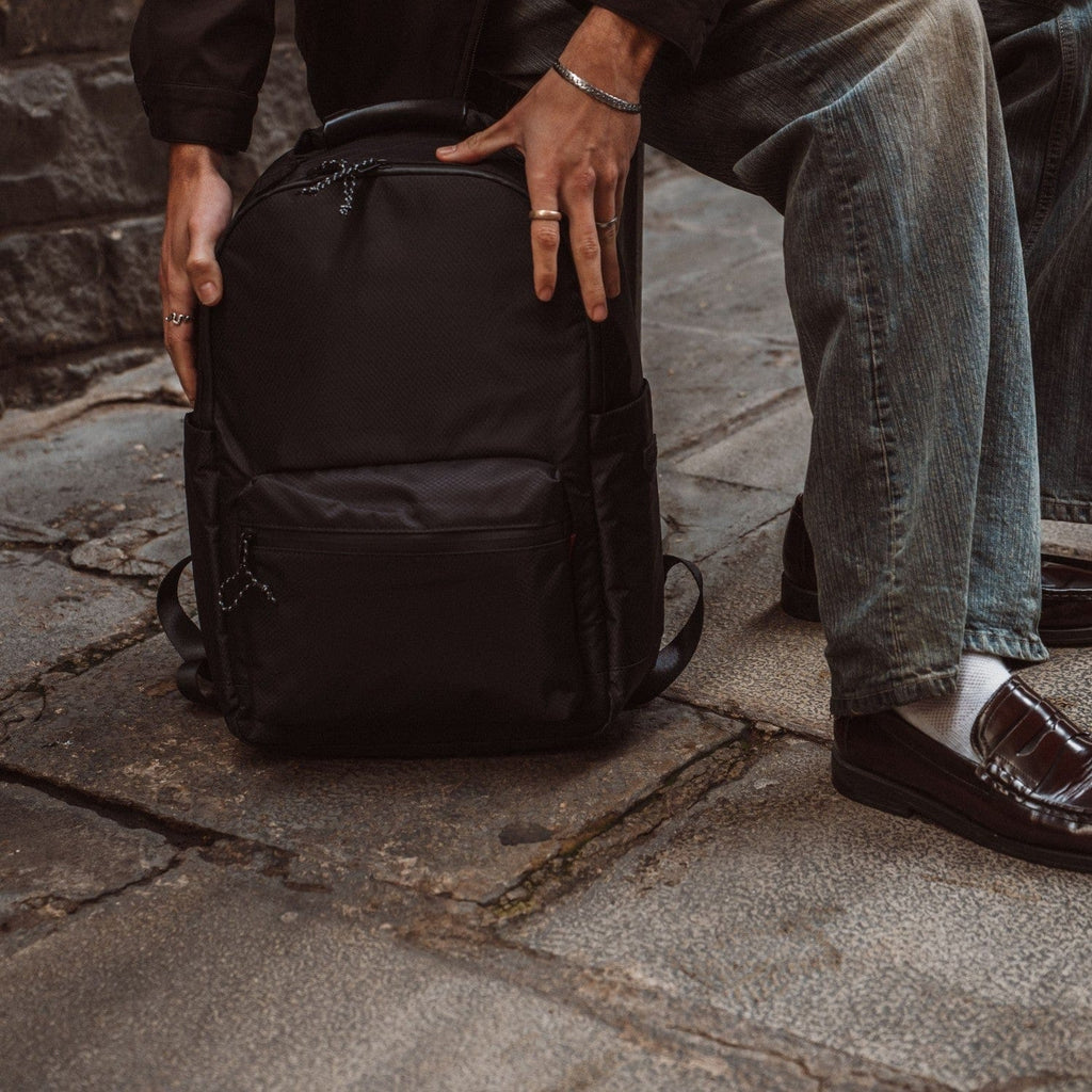 Black backpack with front zipper pocket and padded adjustable shoulder straps.