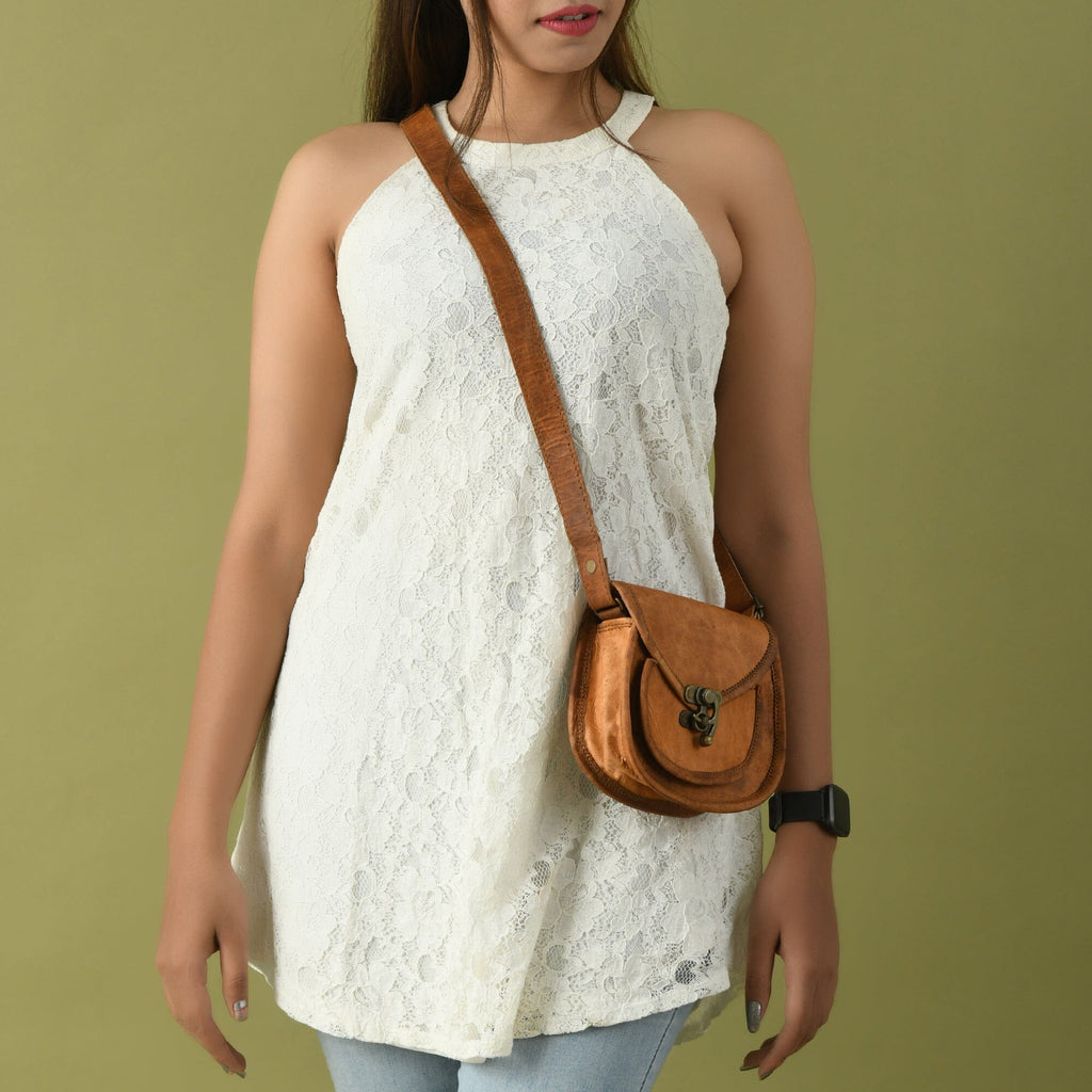 Tan leather crossbody sling bag worn crossbody with front clasp and adjustable strap