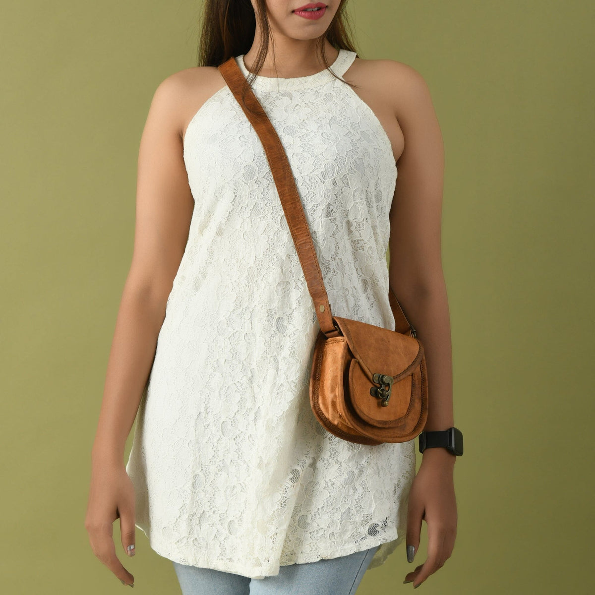 Tan leather crossbody sling bag worn crossbody with front clasp and adjustable strap