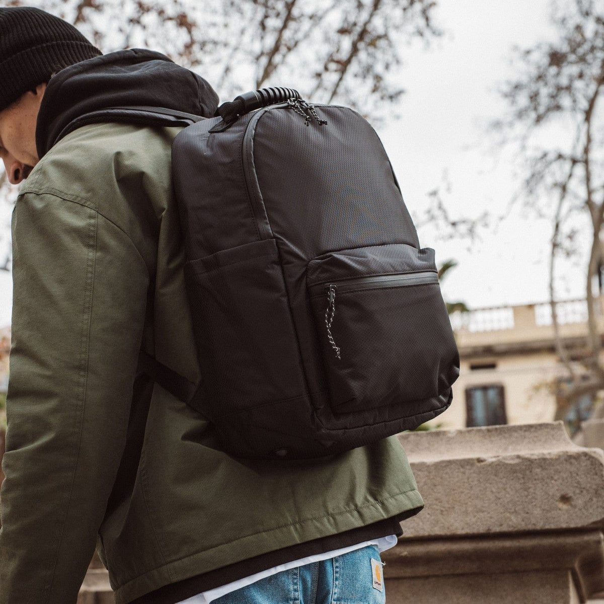 Dark gray-green backpack with front zip pocket and padded side panel.