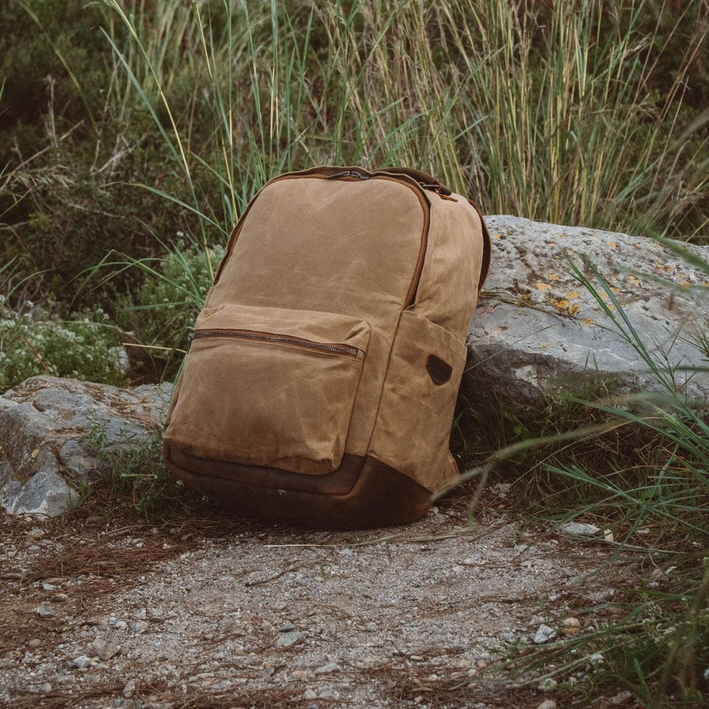 Sand waxed canvas backpack with leather accent panel and front pocket, on rocky ground