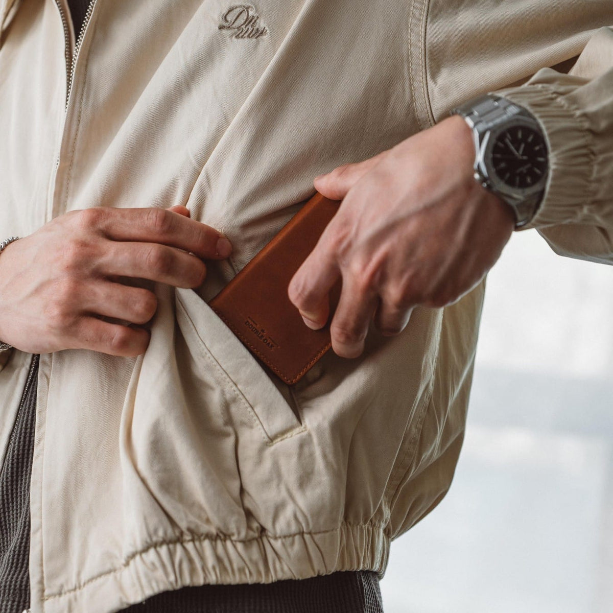 Tan leather bifold wallet in hand with stitched front and embossed logo