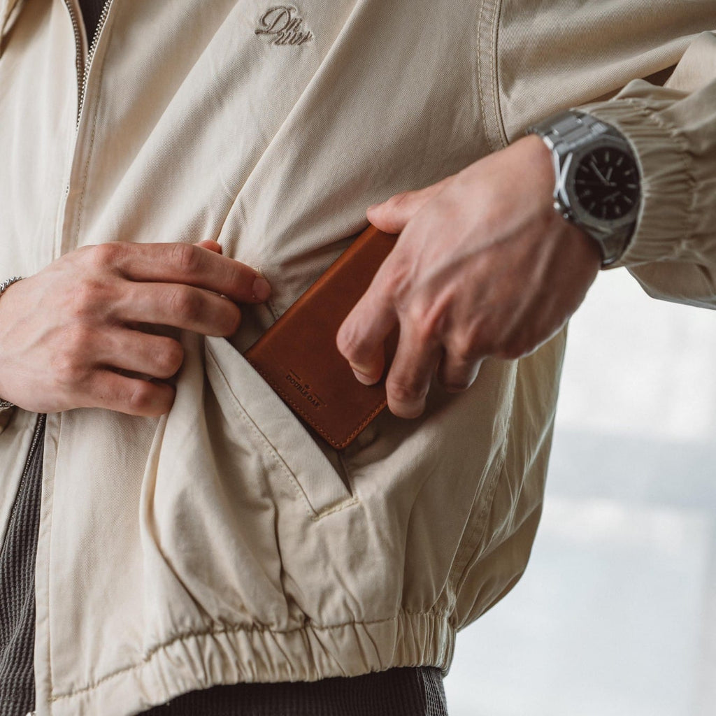 Brown leather bifold wallet shown in hand near jacket zipper pocket.