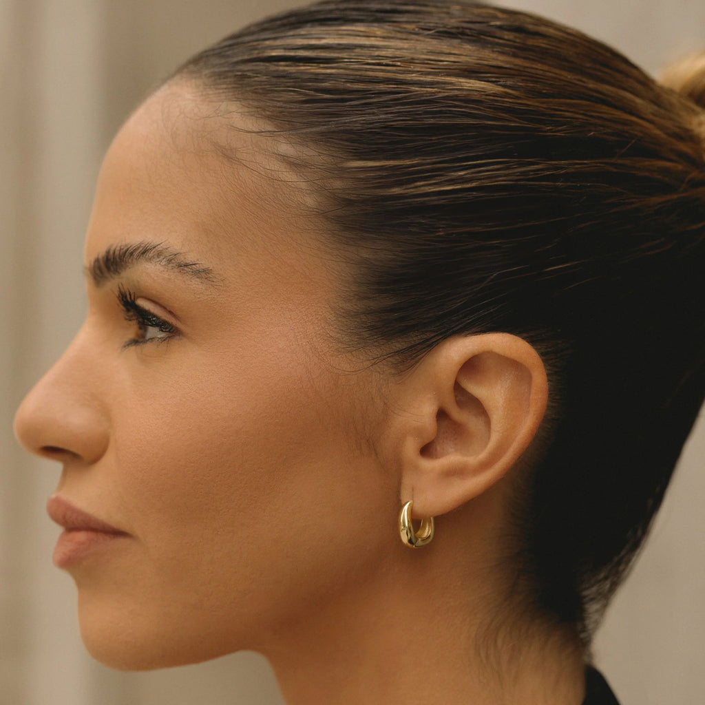 Small gold wavy hoop earrings on ear, polished shine