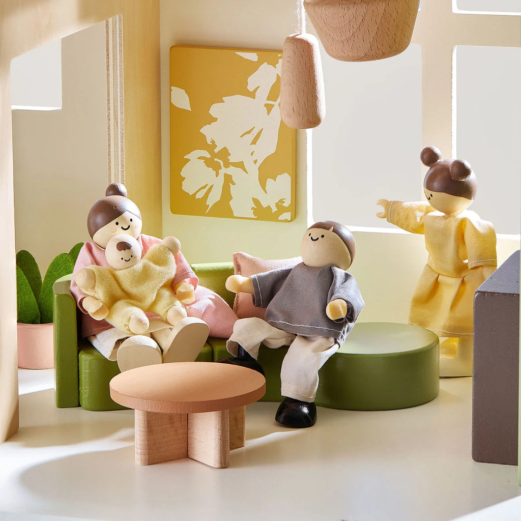 Green dollhouse living area with toy figures, couch, small table, and potted plants
