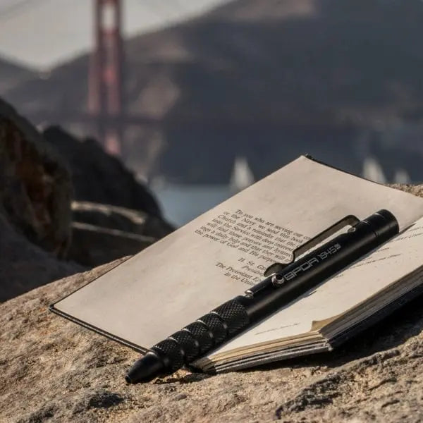 Bolt-action pen with dark body and knurled grip, resting on an open notebook
