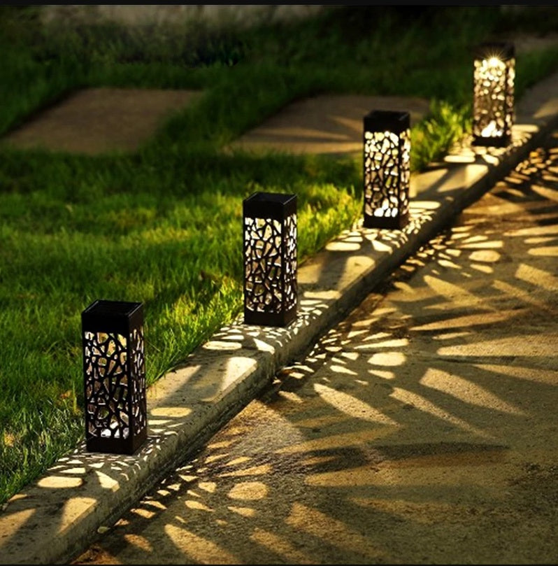 Black solar pathway lantern light with cutout design and ground stake, glowing outdoors