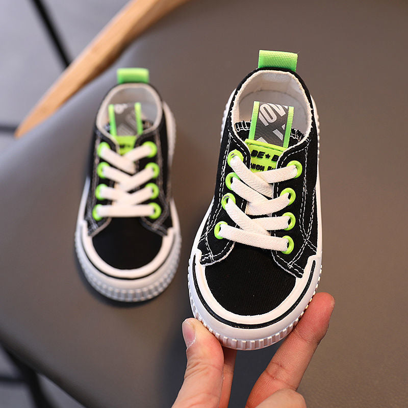 Black kids canvas sneaker with green laces, white sole, and padded collar