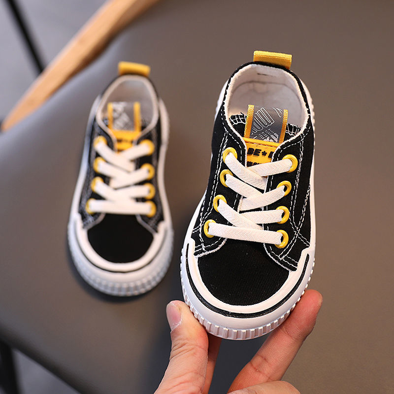 Black kids canvas sneaker with yellow laces, white sole, and stitched toe cap