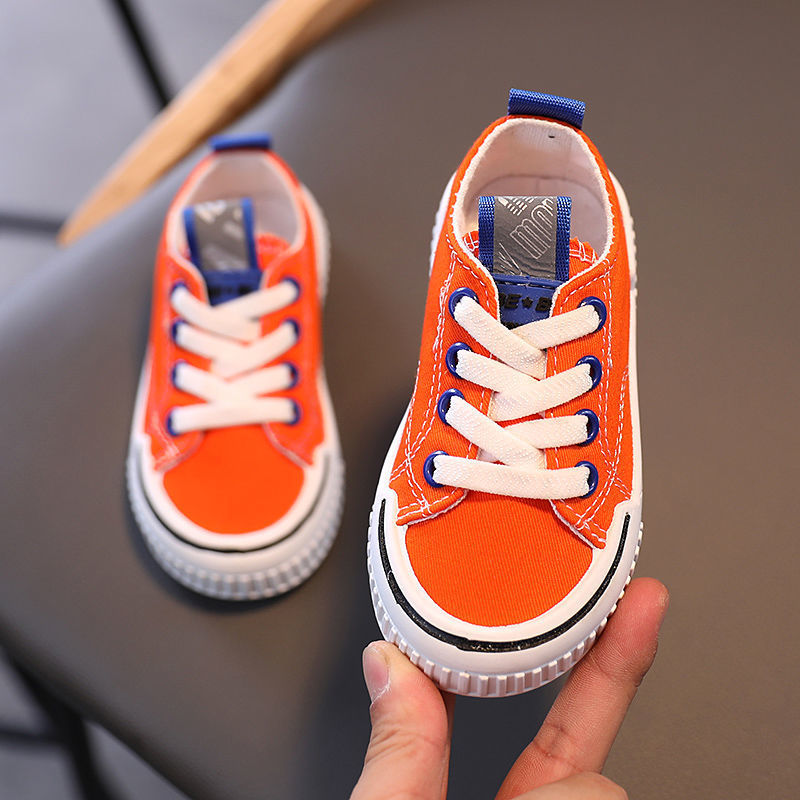 Orange kids canvas sneakers with white laces, white rubber sole, and blue heel trim