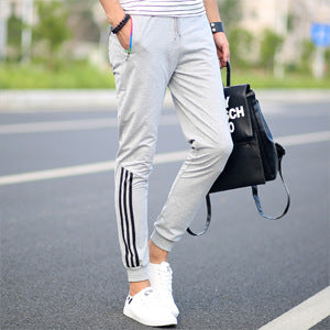 Men's light grey slim casual pants with white triple stripe detail on the leg