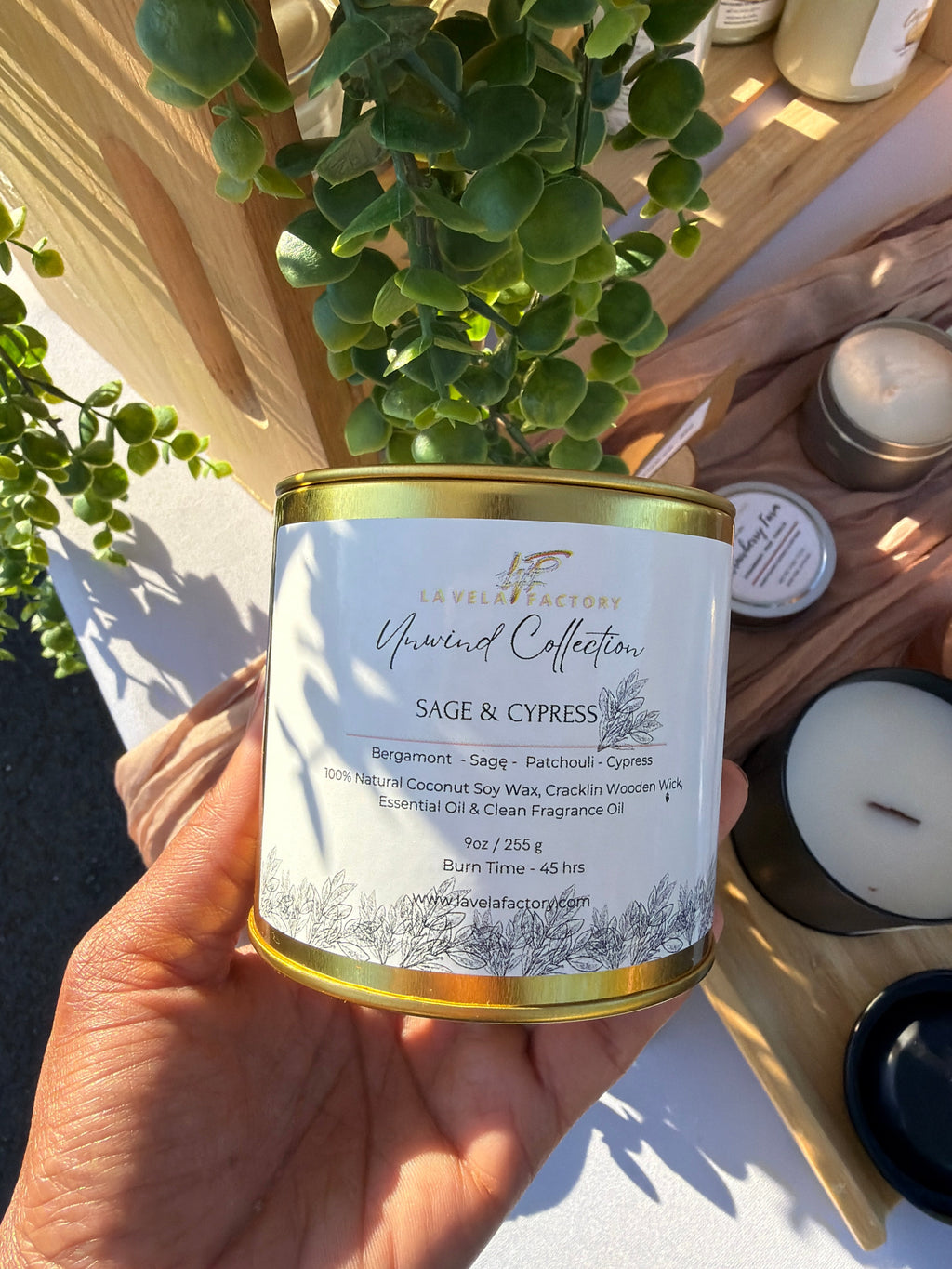 Wood-wick candle tin labeled Sage & Cypress; white wax shown with gold rim.