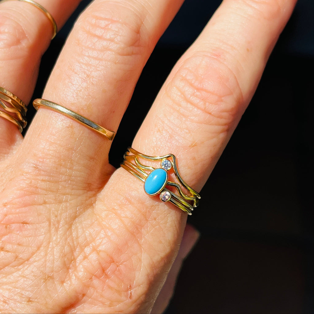 Gold-tone wave ring with oval turquoise cabochon and small clear stone accents