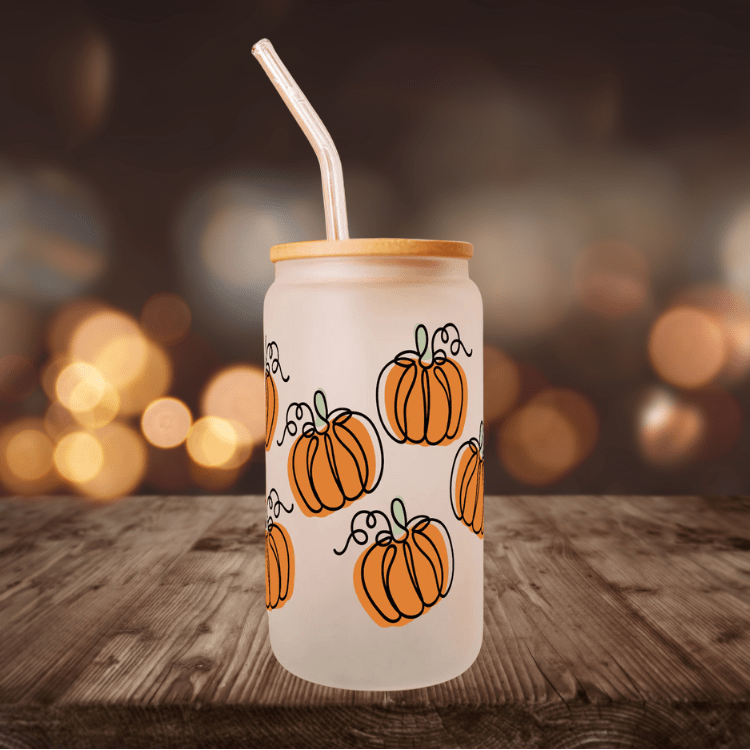 Frosted glass tumbler with orange pumpkin print, bamboo lid and straw on wooden surface