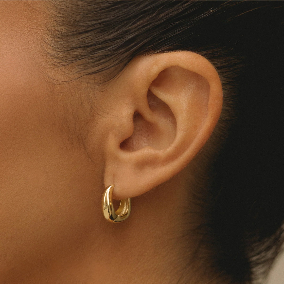 Gold wavy hoop earrings on ear, small hoop silhouette
