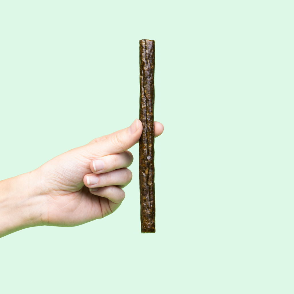 One dark brown beef meat stick held up against a plain background