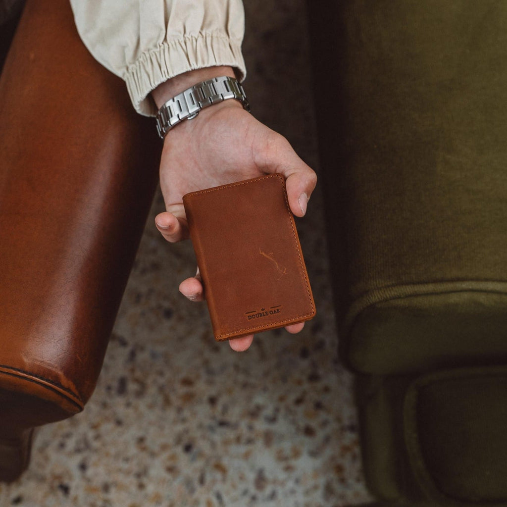 Brown leather bifold wallet held in hand, with stitched front panel.