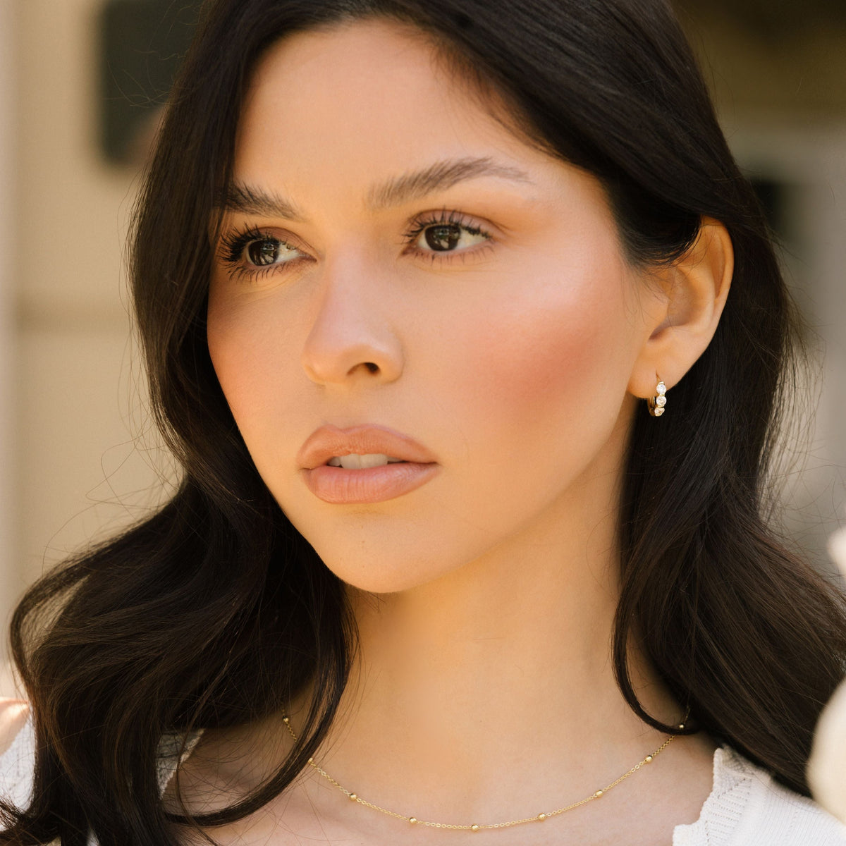 Gold-tone huggie hoop earrings with three clear stones on model