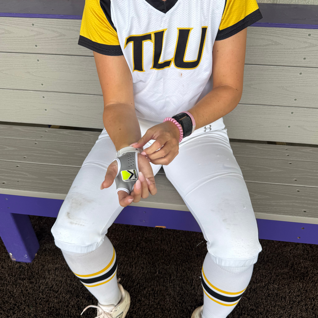 Softball training grip on hand holding a neon ball with gray padded wrist strap