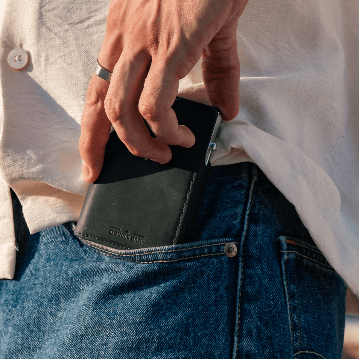 Dark green leather bifold wallet partially pulled from denim jeans pocket