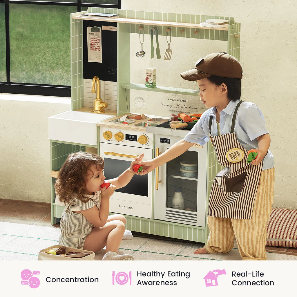 Child using a green kids play kitchen with oven window, sink faucet, and hanging tools.