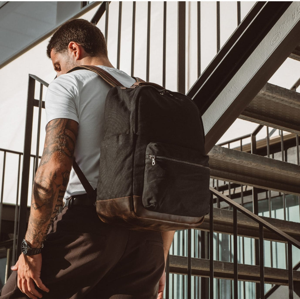 Black backpack with front zip pouch and top handle, worn on person