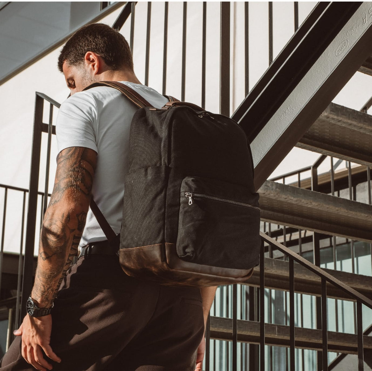 Black backpack with front zip pouch and top handle, worn on person