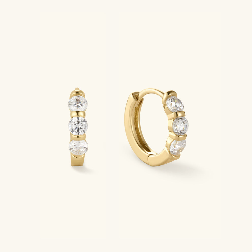 Gold-tone huggie hoop earrings with three clear round stones, front view