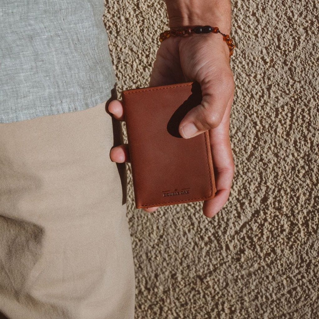 Brown leather bifold wallet with gold clasp and interior card slots, held in hand.