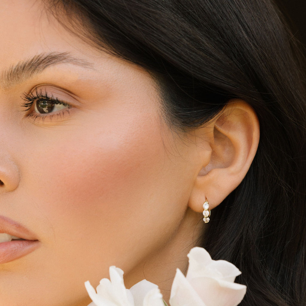 Gold-tone huggie hoop earrings with three clear stones, ear profile close-up