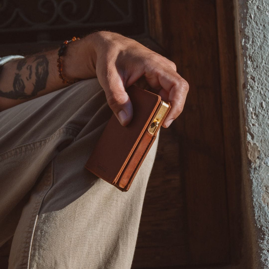 Brown leather bifold wallet with gold clasp detail and card slots, in hand.
